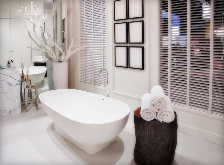 A minimalist bathroom with an earthly element given off by the tree-trunk table. A canto of white tree twigs serve as the transition from white minimalist to modern rustic aura. The central tub is the focal point . The six blank frames add visual height while the far side wall - covered with mirror from floor to ceiling- magnifies the spatial orientation of the room.