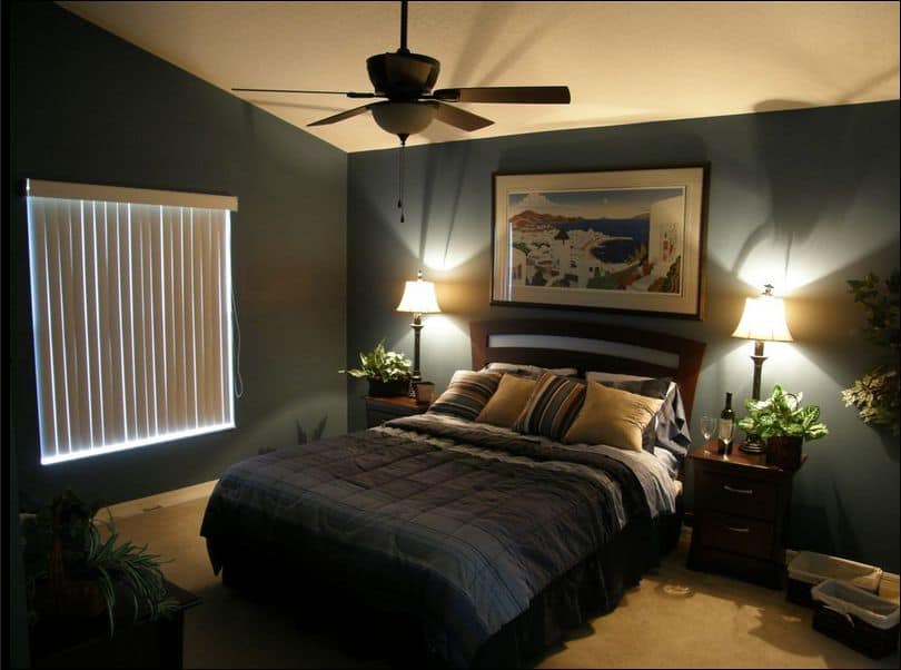 A masculine bedroom with deep blue accent and dark relaxing atmosphere. Deep wooden furniture and potted greenery along with a large framed paining pop in this awesome master bedroom.