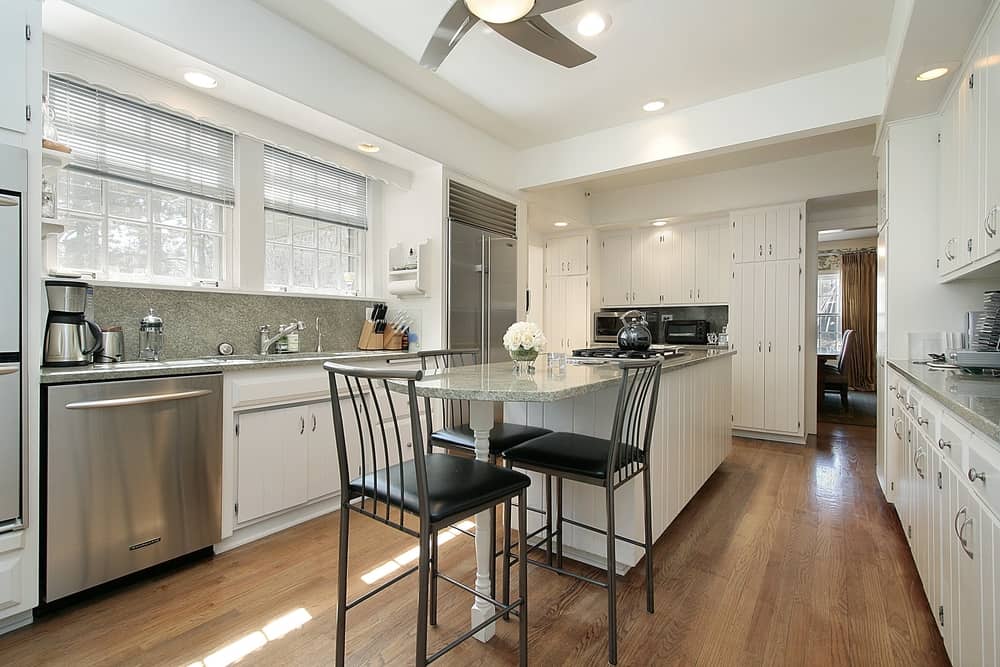 This white kitchen has a large island-cum-dining space placed in the middle. The countertop is made of grey marble . Many of the modern day kitchen ideas revolve around white laminated cabinets because of the sheer beauty that they bring into a kitchen. Also, the brushed aluminum are strategically selected to give a fancy look to the kitchen.