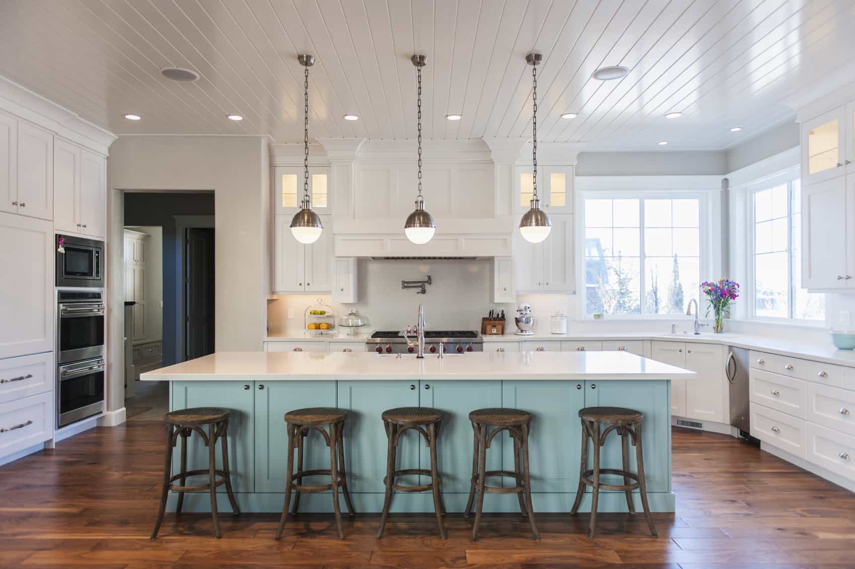 Bright contemporary kitchen featuring white and wooden color. The sky blue island is quite large with white marble countertops and low-hanging lights.