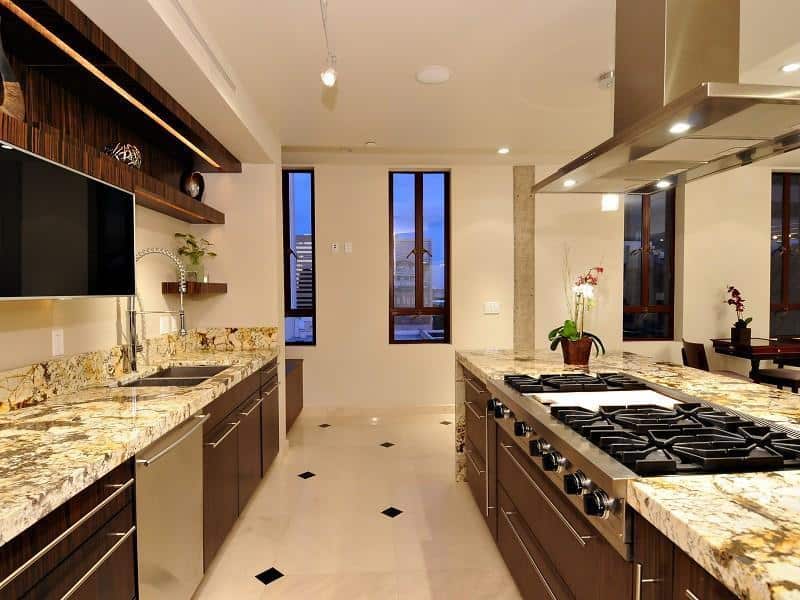 A luxury kitchen with random patterned granite countertops catching attention of the viewers. The kitchen cabinets are made of dark wood that conforms to the modern mood of this kitchen .