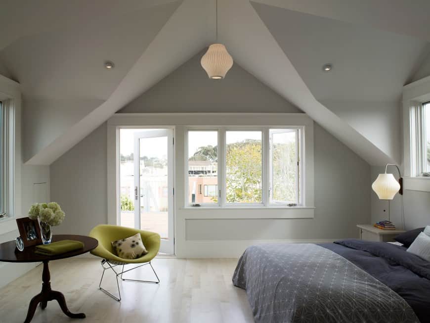 A light and soothing bedroom with dove grey walls. The bed creates a navy blue accent . The light pale wooden floor and walls reflect much of the available light making the room open.