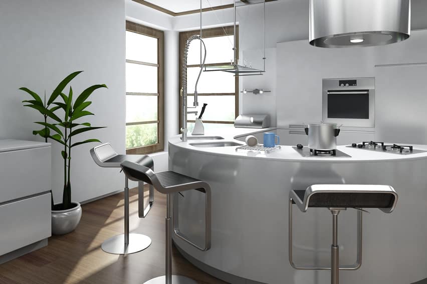 A small modern corner kitchen with a circular main area . The semi-circular kitchen counter laminated in white is the main working area – which also supports a seating arrangement with high chairs .
