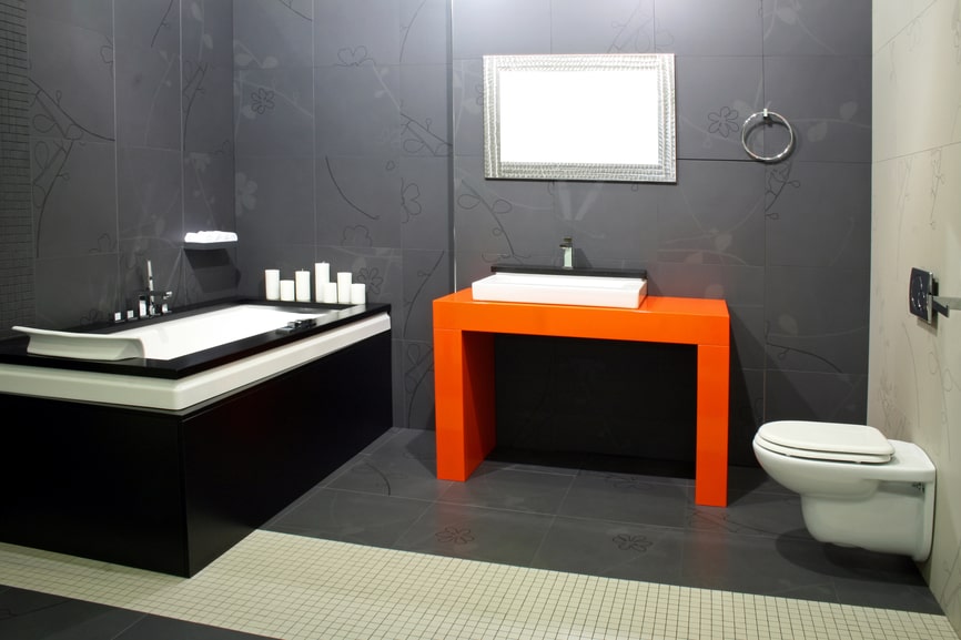 An incredible modern bathroom with white & black tub and orange sink pedestal holding the small white sink in place.