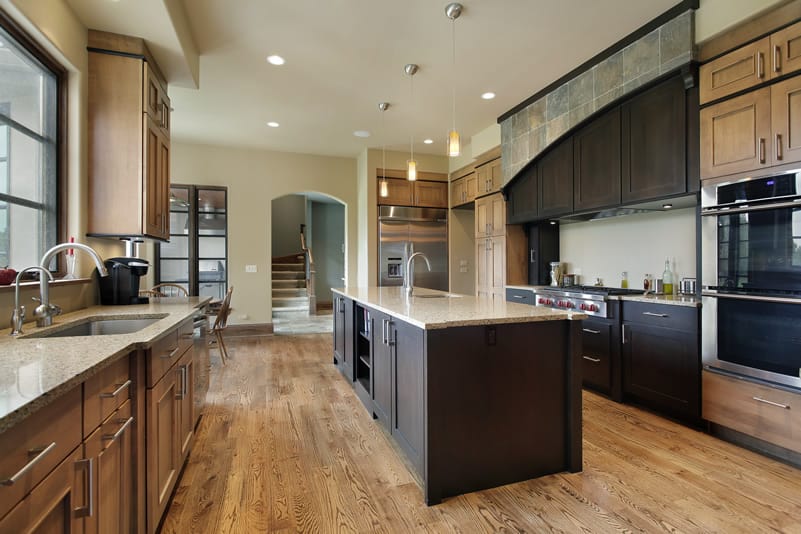 A quite contrasting yet luxurious long kitchen that uses various colors and grades of wood to create a modern kitchen. The natural wooden floor and white wall lengthens the room. The dark colored cabinets and island livens up the room by creating a splendid contrast. The light color of marble countertop makes the dark colors pop even more.
