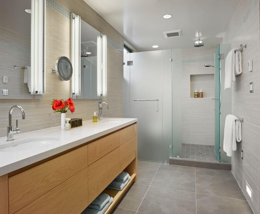 A majestic neutral bathroom of wood and tiles. The shower enclose are made of frosted glass while the vanity is wooden with laminated white countertop.