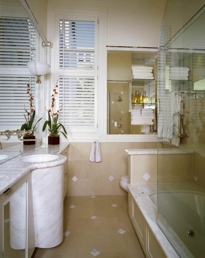 A small bathroom with nicely crafted small white marble tiles in between beige tiles . The cylindrical sink is the main focus of attention of this bathroom.