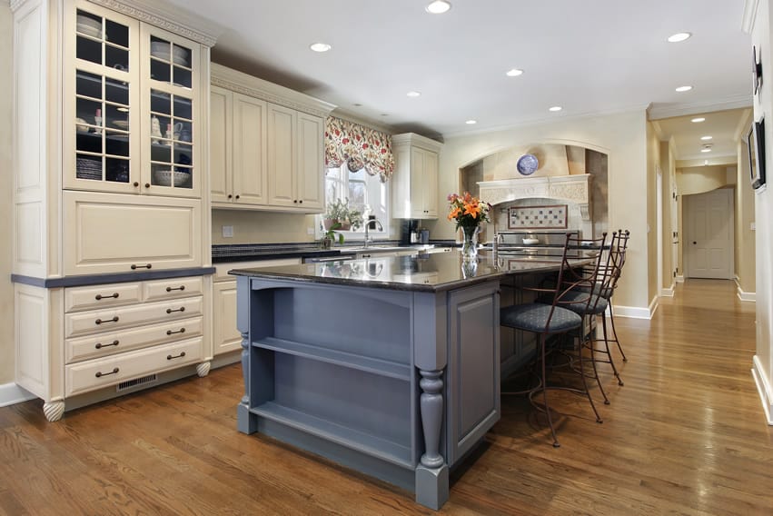 This exclusive kitchen uses bold combination of different colors and textures. While the floor is made of Golden Oak planks, the island is indigo and the kitchen has off-white cabinets. The countertop is made of black granite . The coloring of  upholstery of bar stools matches that of island .