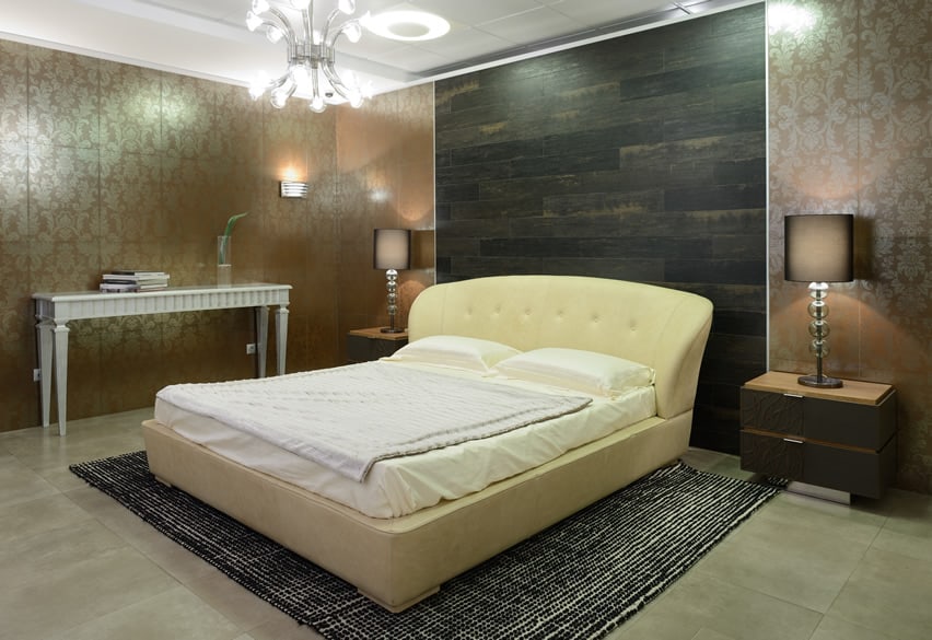 A nice bedroom with yellow white bed. The finishing used in different pieces are both smooth and rough that creates diversity . The floor has ceramic tiles with concrete finishing . The wall use golden colored stainless steel finishing. The wall behind the head of bed uses horizontally stained black wood.