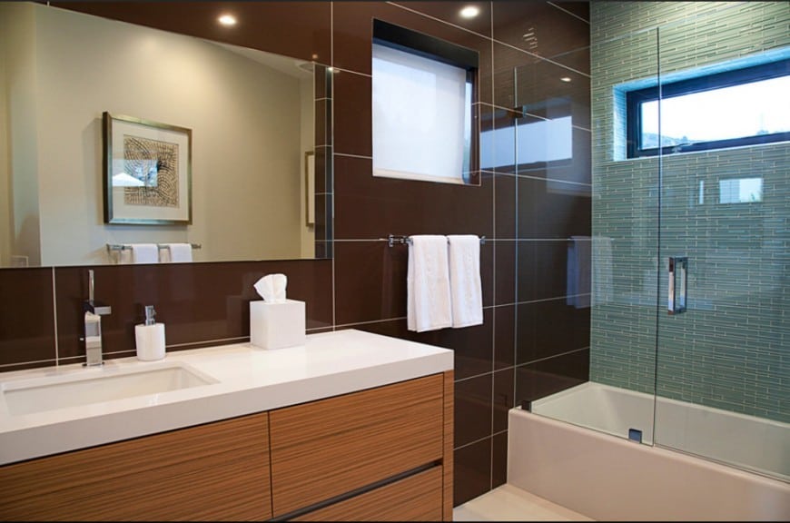 A cool combination of deep colors make this bathroom stand out. Brown wall tiles leads into the glass-enclosed bathtub and to the aqua blue tiles. The upper window allow plenty of natural light to come in.