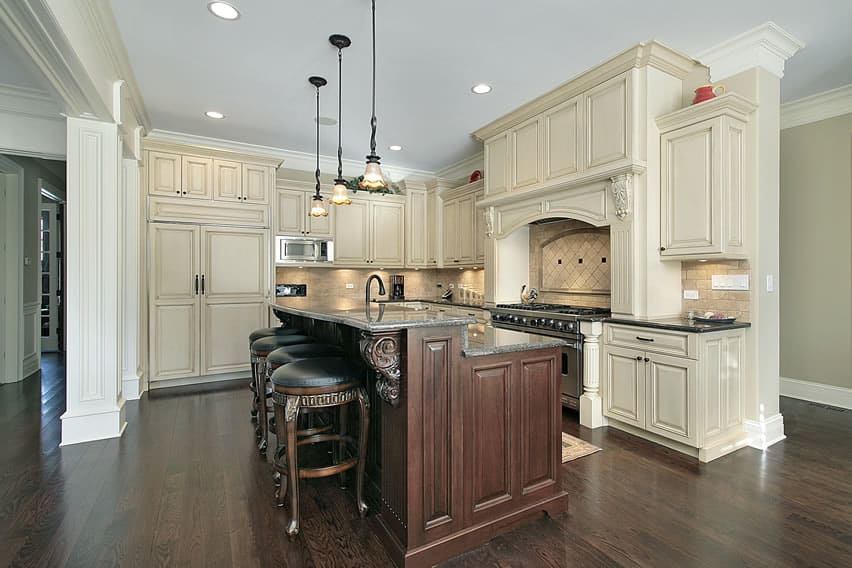 A L-shaped kitchen with neo-classic designs . The light cream colored cabinets have matching backsplash and false columns. The island is quite polar with dark cherry wood matching the walnut deep-colored floor. The black counters match the fixtures and appliances.