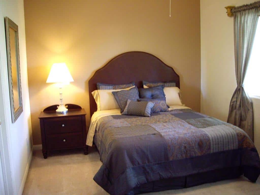 This small bedroom makes use of dark colored bed and side table while the wall is light orange.