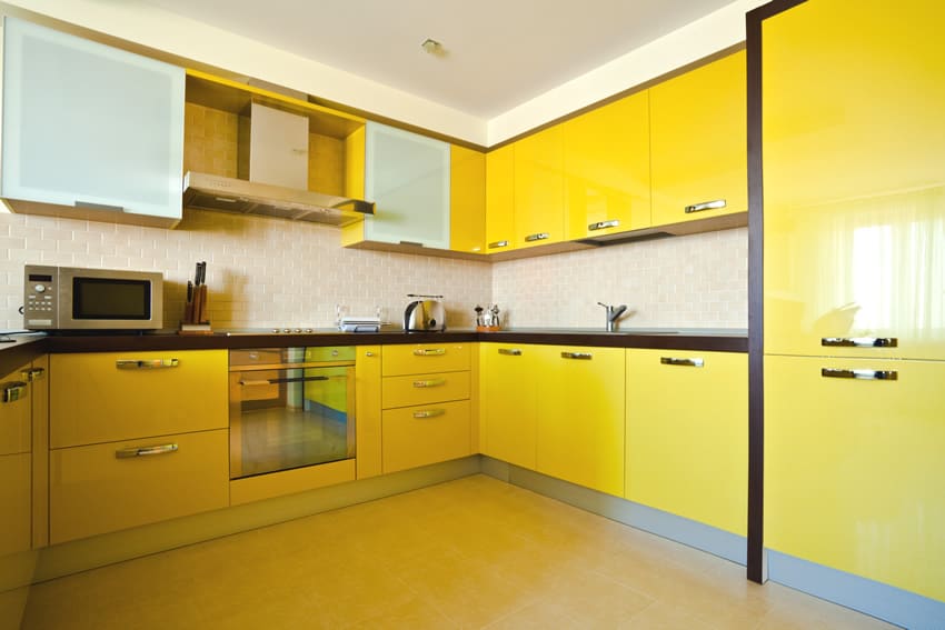 A simple uneventful kitchen lightened up by the bright yellow color used in the kitchen cabinets. The black countertop and light beige backsplash tones down the yellow glow while the glass door adds some texture to this kitchen .