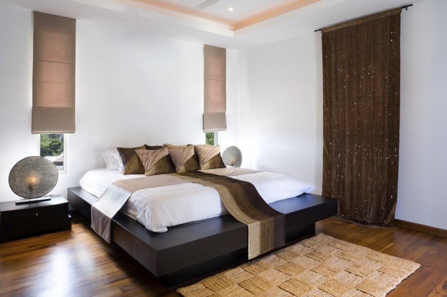 A modern exquisite bedroom full of simplicity and having rich brown tones. While the black bed and brown curtains pop extremely well , the textured rug and bed covers add some depth to the cheerful room.