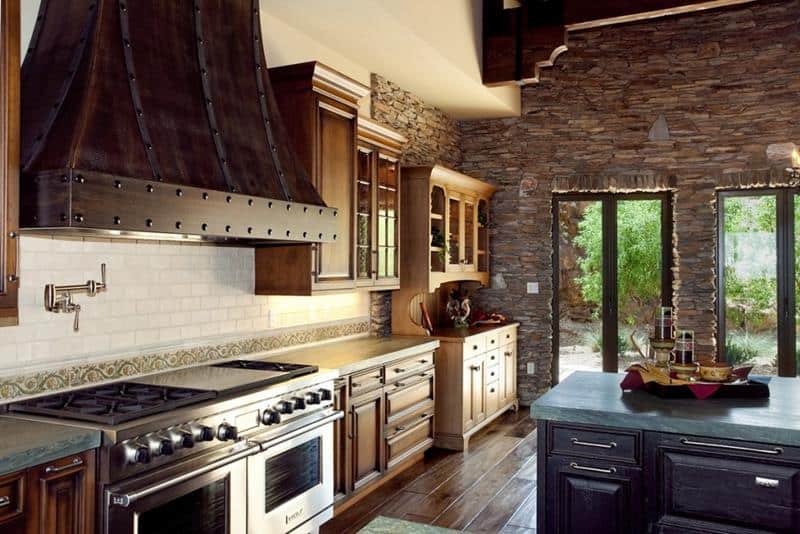 Finally a kitchen with copper hood and exposed stone on the back wall . Exposed bricks are used in the far side wall as well.