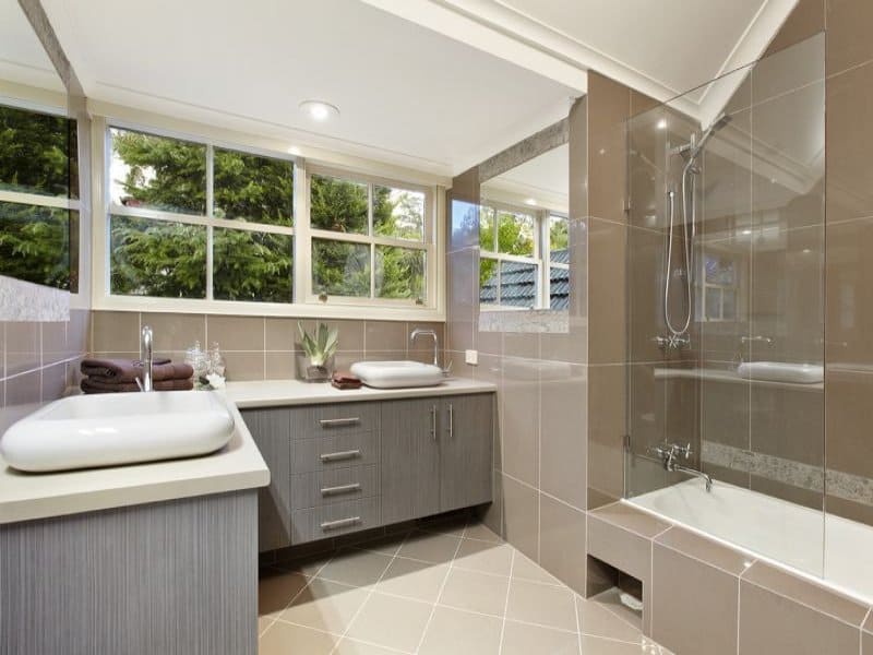 Large windows are seldom used in bathrooms, but when used, they can bring in lots of natural light and brighten the bathroom. The Zorba colored wall tiles and diagonal floor tiles complement with natural gray colored cabinets . 