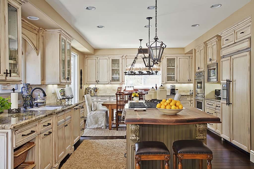 Delightful traditional kitchen that features deep cream color in walls and cabinets . The floor is dark wooden. The large island is topped by dark wooden countertop.